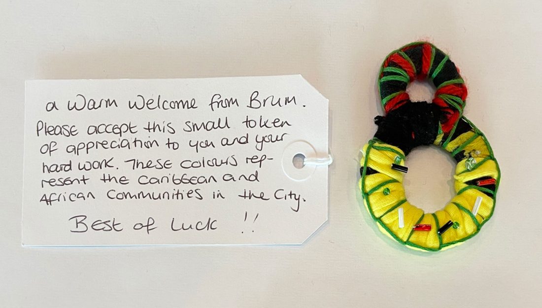 a handmade textile object made up of two rings of yellow, red, black and green yarn sits on a white background next to a hand written gift tag