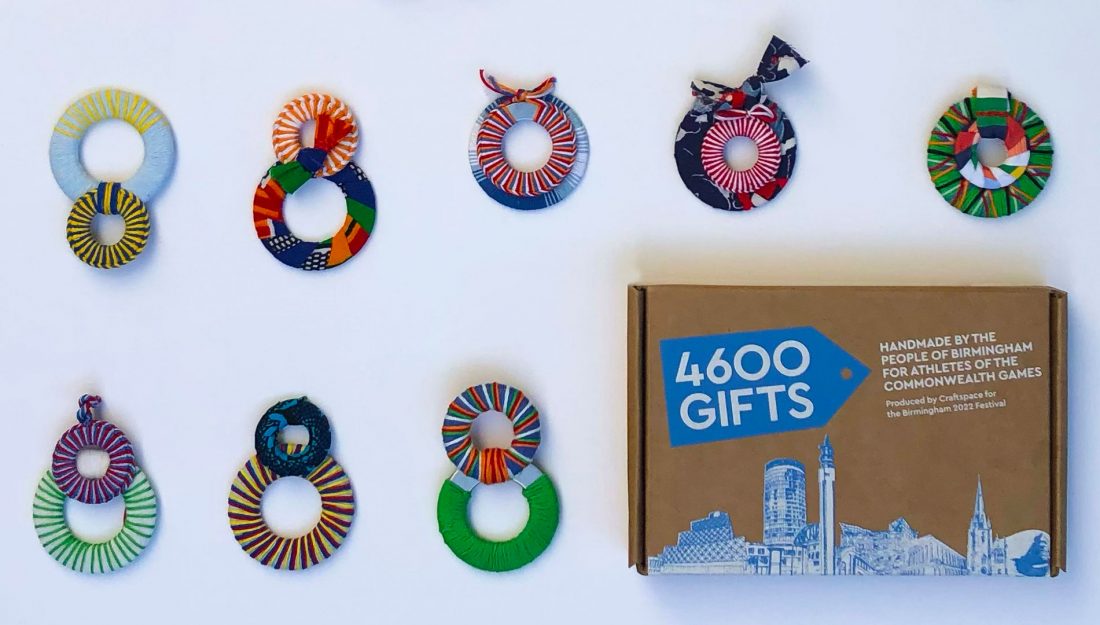 a selection of eight handmade textile objects made up of two rings wrapped in colourful yarn are laid out next to a brown box with blue and white graphics on it.