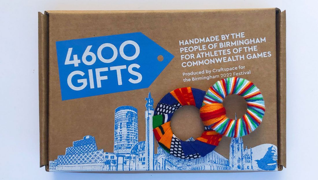 a handmade textile object made up of two rings wrapped in colourful yarn sits on a brown kraft box with blue and white graphics printed on it.