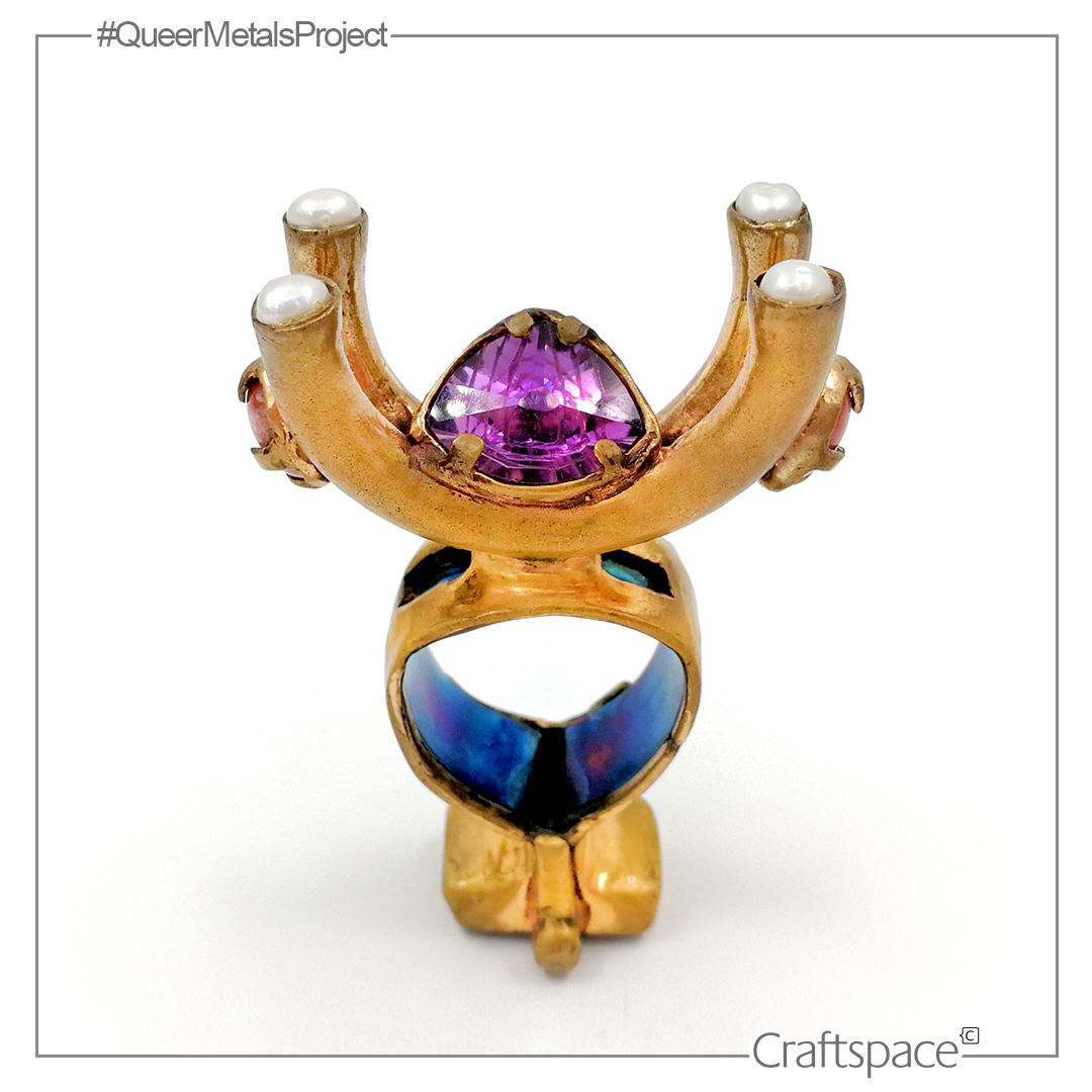a sculptural, gold-coloured ring with four pearls at the top of curved antler points, a purple faceted stone cradles in the curve. The internal section is blue.