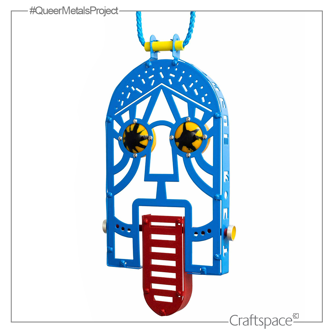a blue abstract geometric face shaped like an arch with a red tongue and yellow eyes. A pendant hanging from a blue cord.