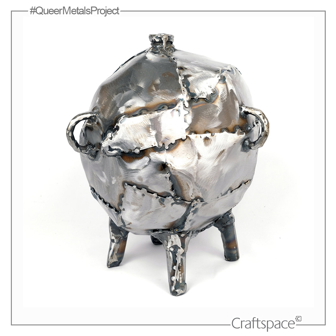 a round shiny metal vessel with stubby feet and handles made up of patchwork metal pieces