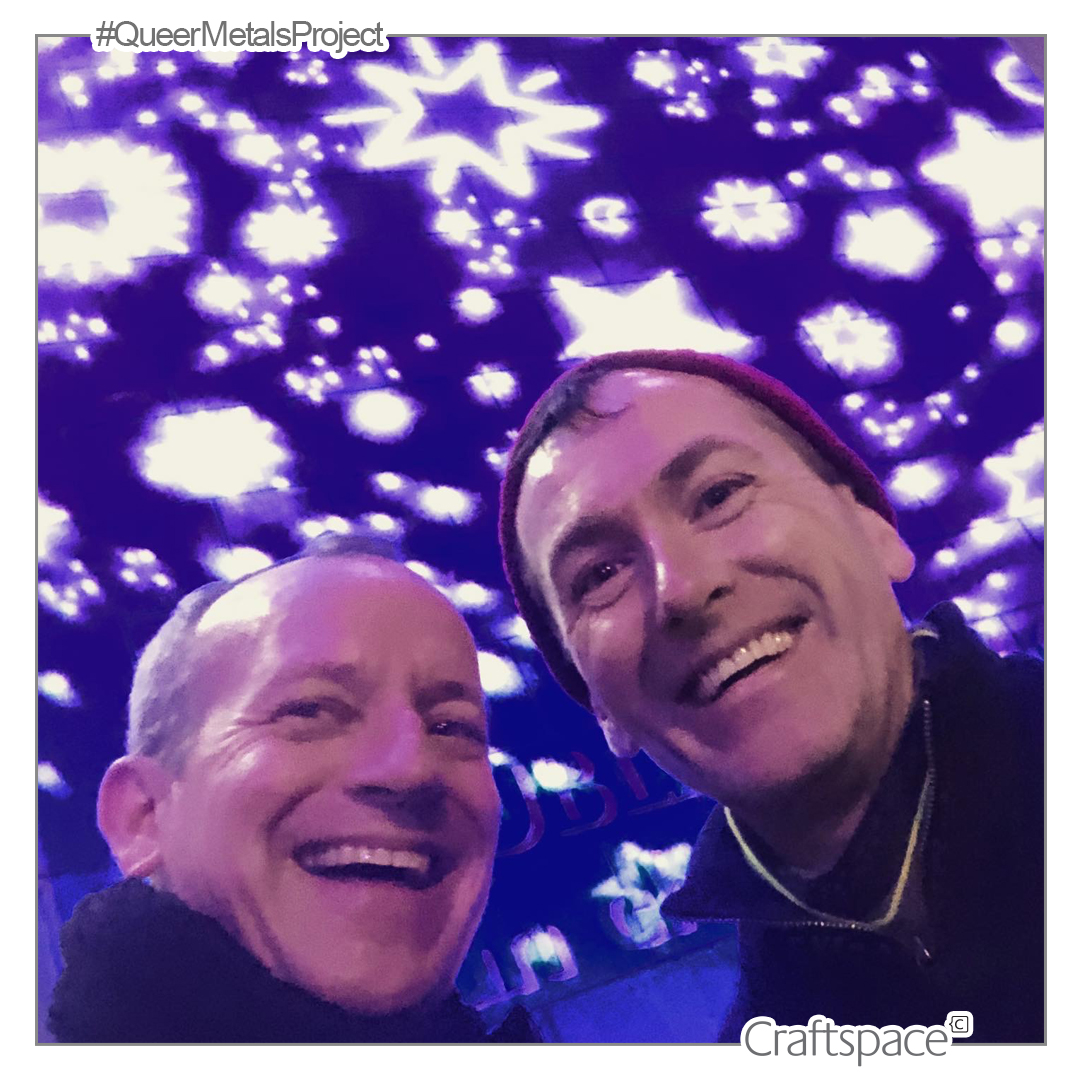 Against a blue ceiling with white stars of light, two men laugh into the camera