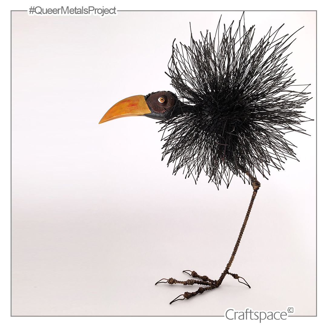 A fluffy bird made of steel wire stands on one foot, it's oranged beaked head juts out around it's body.
