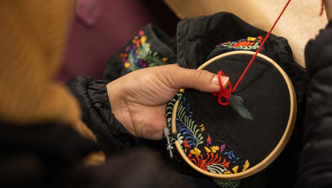 a hand is visible holding an embroidery hoop on a black textile item which is being stitched with red cotton.