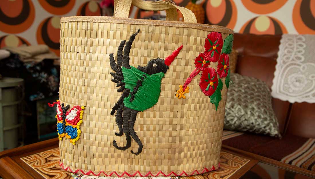 a woven straw basket decorated with a bird, flowers and butterfly sits on a table in a 1960's front room