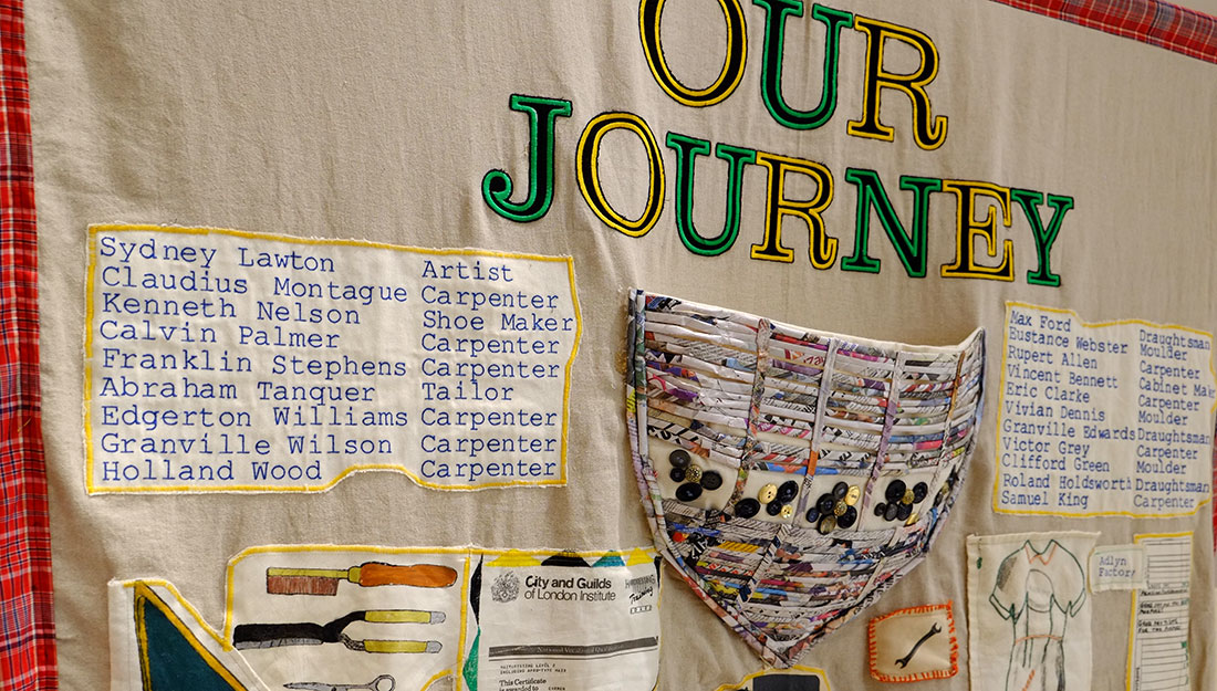 A large embroidered wall hanging. In large letters it says 'our journey' and there is a list of names and professions beside an embroidered section which looks like the bow of a boat, such as the Windrush.