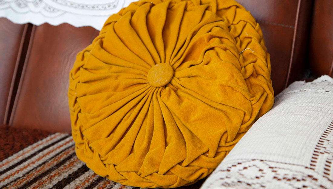 A round, mustard coloured, velour pleated cushion on an old fashioned sofa.