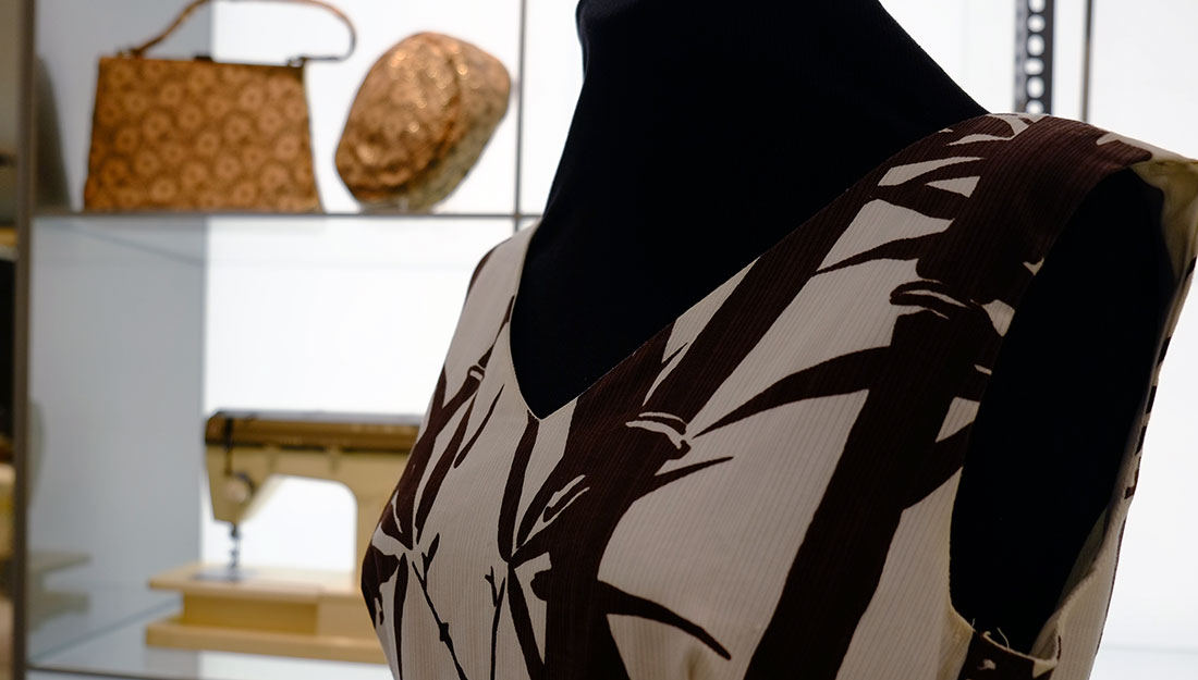In the foreground, part of a dress with a graphic bamboo pattern on it. In the blurred background is a sewing machine and a vintage handbag.