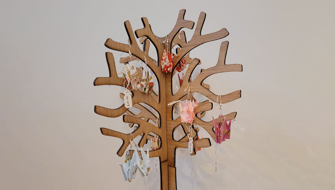 a wooden jewellery stand in the shape of a tree holds pairs of colourful paper earrings