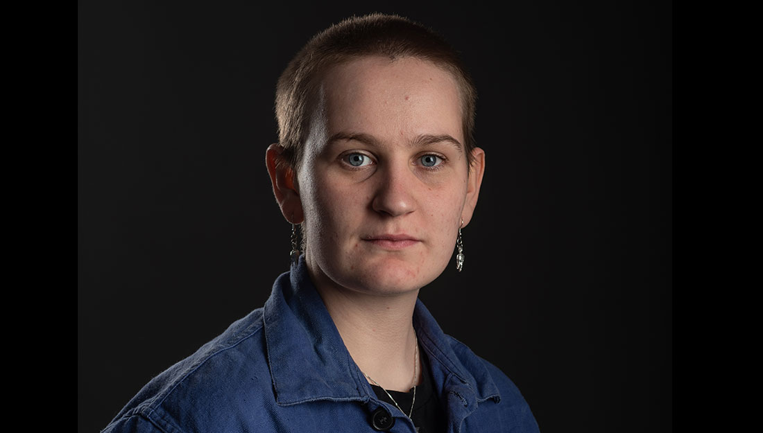 Portrait of Annie Higgins. Wearing very short hair, earrings and and blue boiler suit.