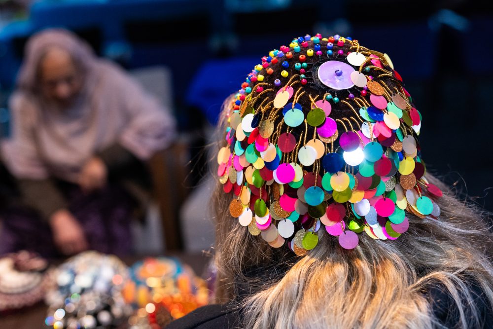 A woman wearing a brown velvet Kurdish women's cap made by Zohra, embellished with colourful, metallic and sparkly plastic discs suspended on beaded threads.