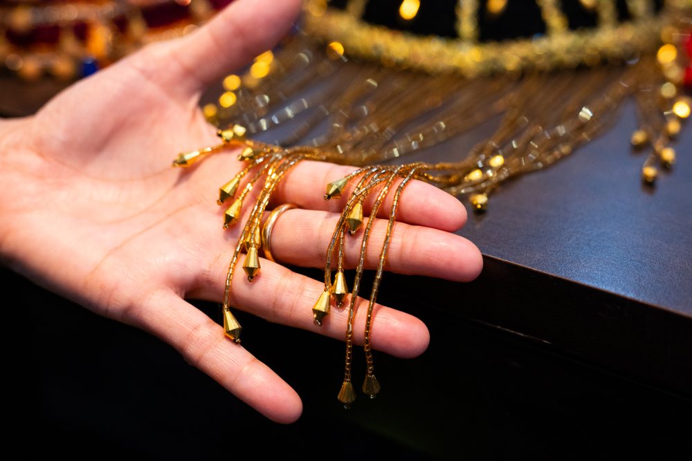 A close up photograph of the trim on a Kurdish womans cap made by Zohra. There is a curtain of beaded threads, each finished with a large gold bead.